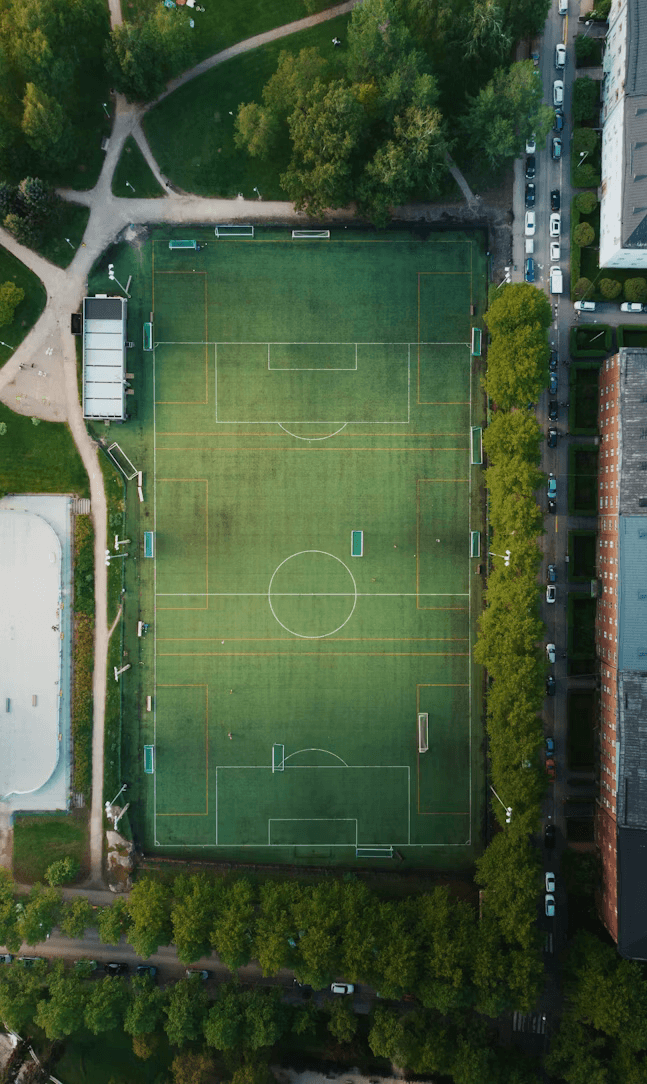 Aerial view of football pitch surrounded by trees and urban landscape